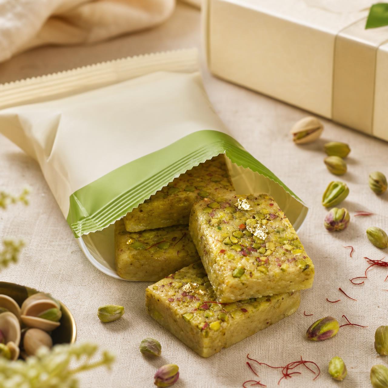 Open pistachio cardamom NAYI wrapper with barfi bites, pistachios, cardamom and saffron